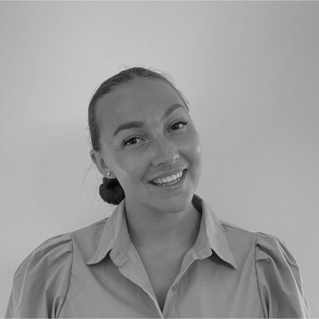 Smiling woman with hair in a bun wearing a light button-down shirt, posed against a plain background.